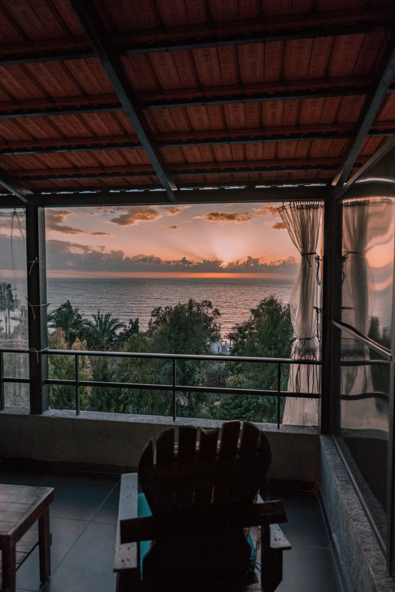 The covered balcony at Paradise Sunset in Byblos, looking over the trees to the sea at sunset